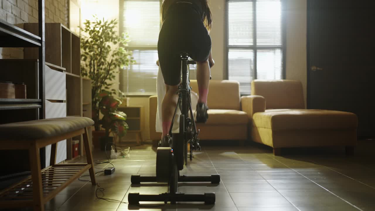 亚洲女人骑自行车。她正在房子里锻炼，一个骑自行车的亚洲女人。她正在房子里锻炼。视频素材