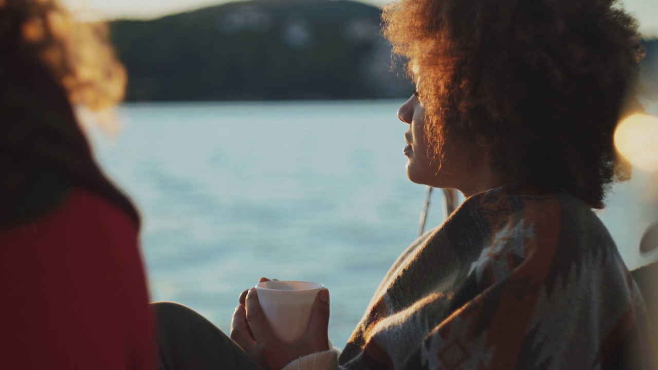 日落时分，一名年轻女子在帆船的甲板上喝视频素材