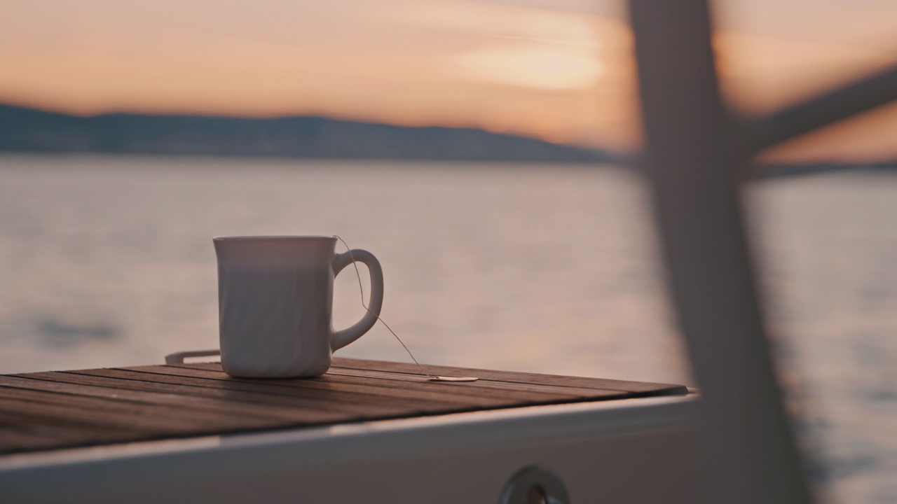 黄昏时分，在一艘帆船的木制船尾上，一杯茶缓缓升起视频素材