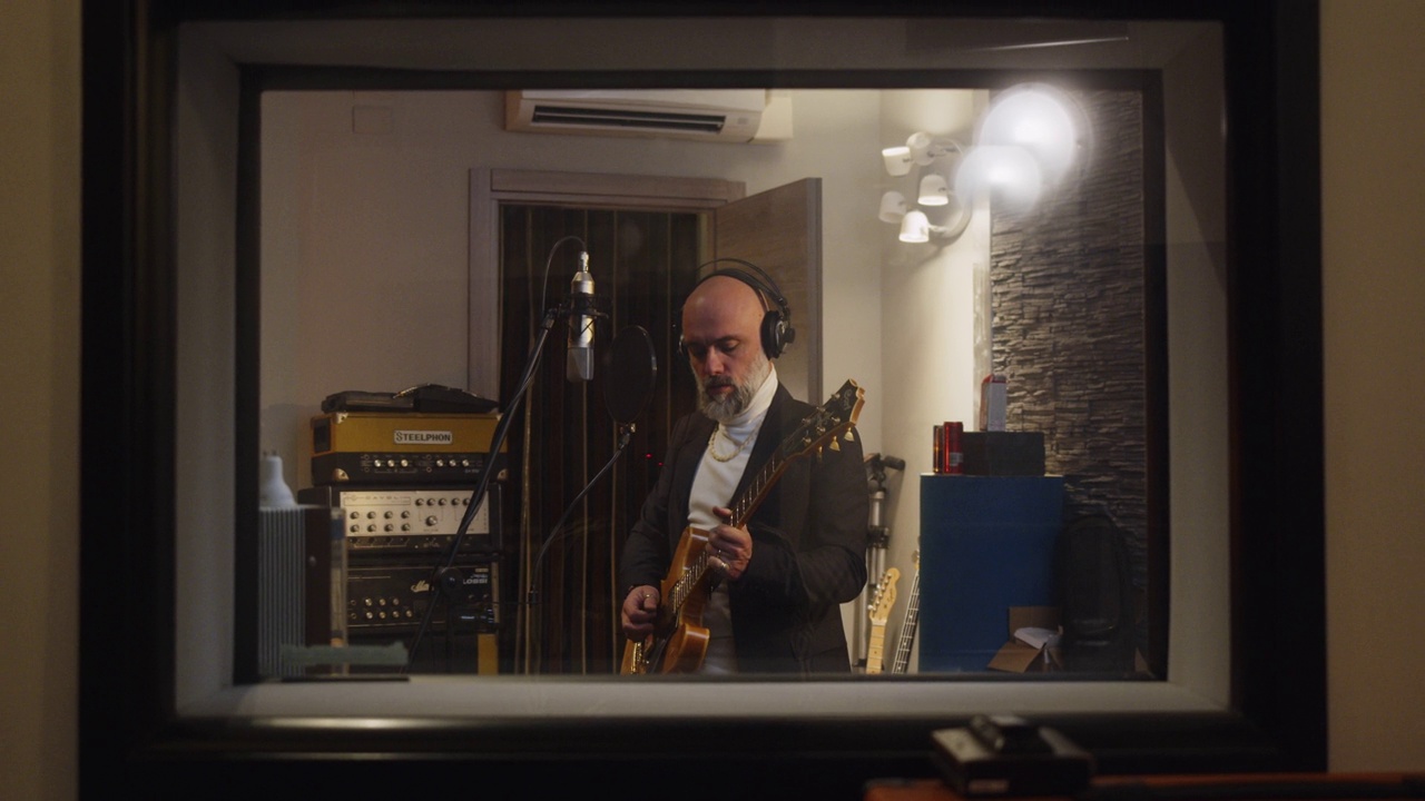 一位歌手一边唱歌一边弹吉他，在一个专业的录音棚里录制音乐视频下载