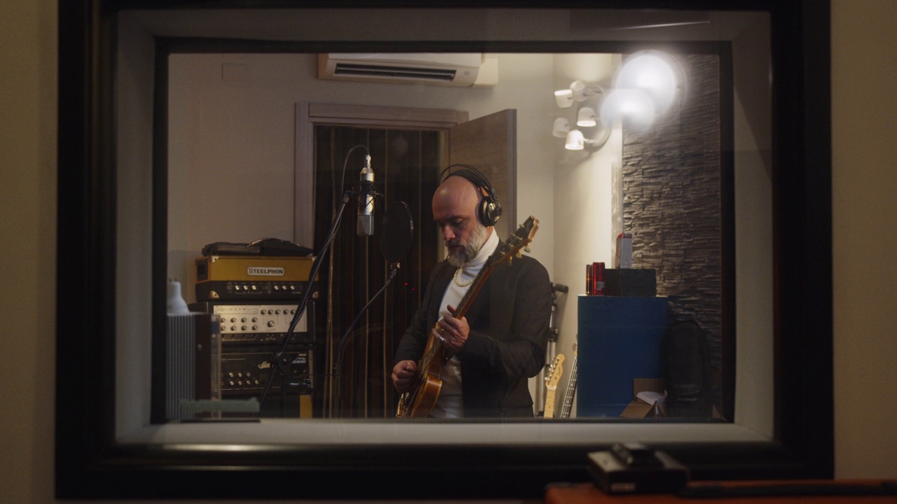 一位歌手一边唱歌一边弹吉他，在一个专业的录音棚里录制音乐视频下载