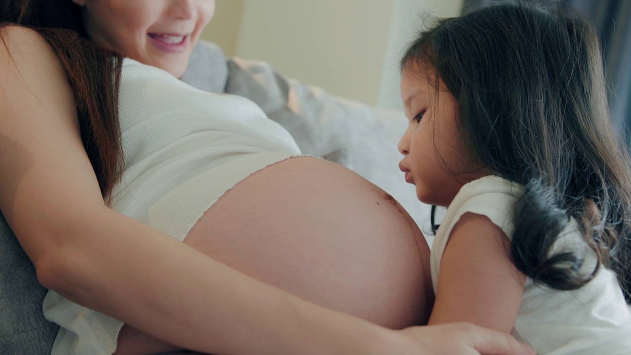 快乐可爱可爱的蹒跚学步的女儿在家里拥抱和亲吻怀孕的母亲。视频下载