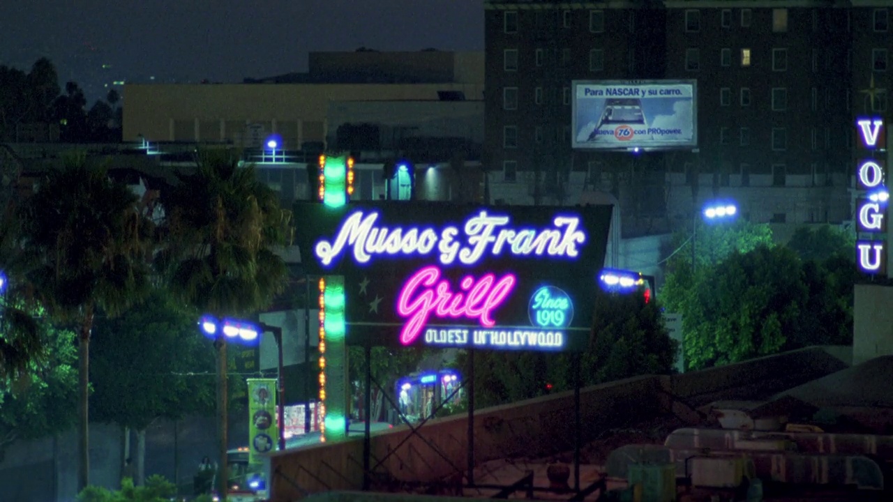 从停车场向右向左移动到“musso & frank grill”的霓虹灯招牌。餐厅。屋顶通风口。在bg，棕榈树，灯光和霓虹灯招牌的商店。好莱坞的大街。地标性建筑。城市区域。视频下载