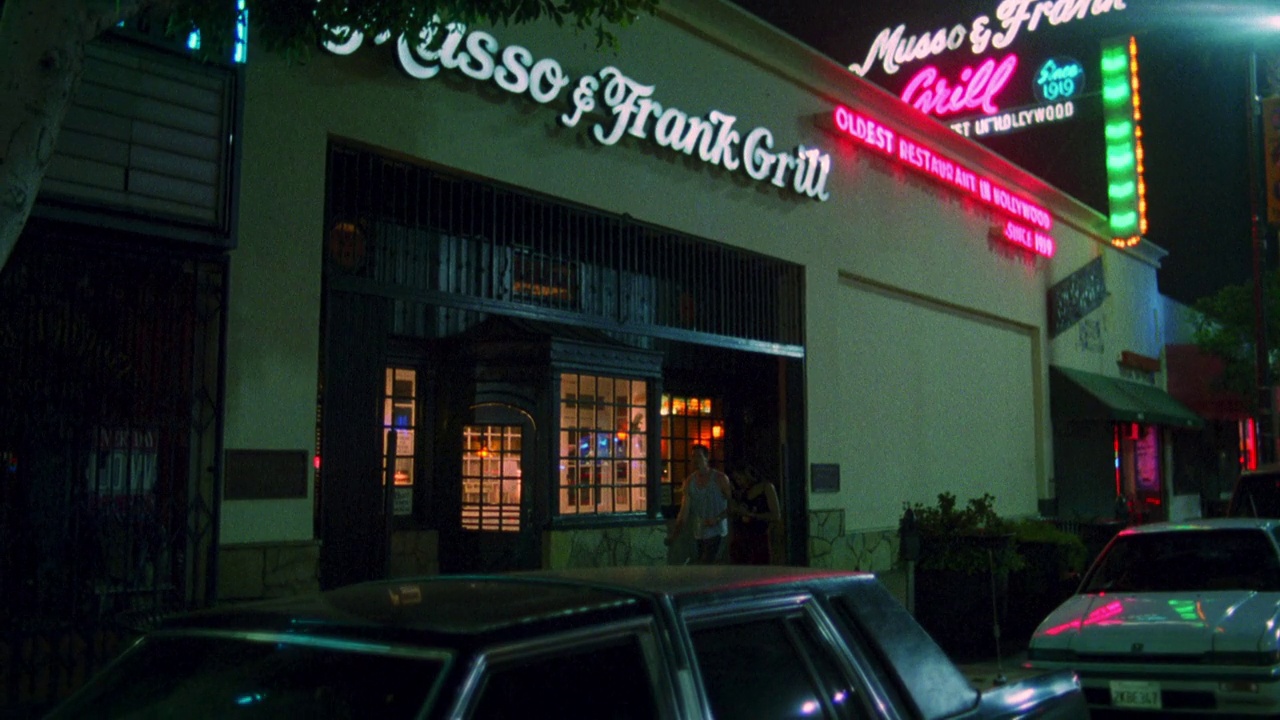 中角的“musso & frank grill”餐厅招牌。餐厅入口上方的“musso & frank grill”霓虹灯招牌。人们走在人行道上。停着的汽车。好莱坞的大街。视频下载