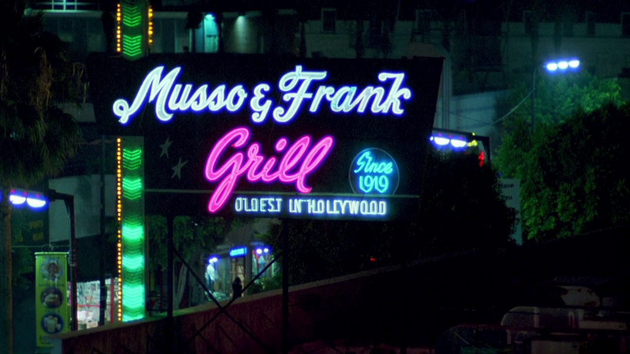 从“musso & frank grill”的广告牌从右到左，到霓虹灯招牌“musso & frank grill”。好莱坞的大街。bg的灯光和商店。有通风口的屋顶。城市区域。视频下载