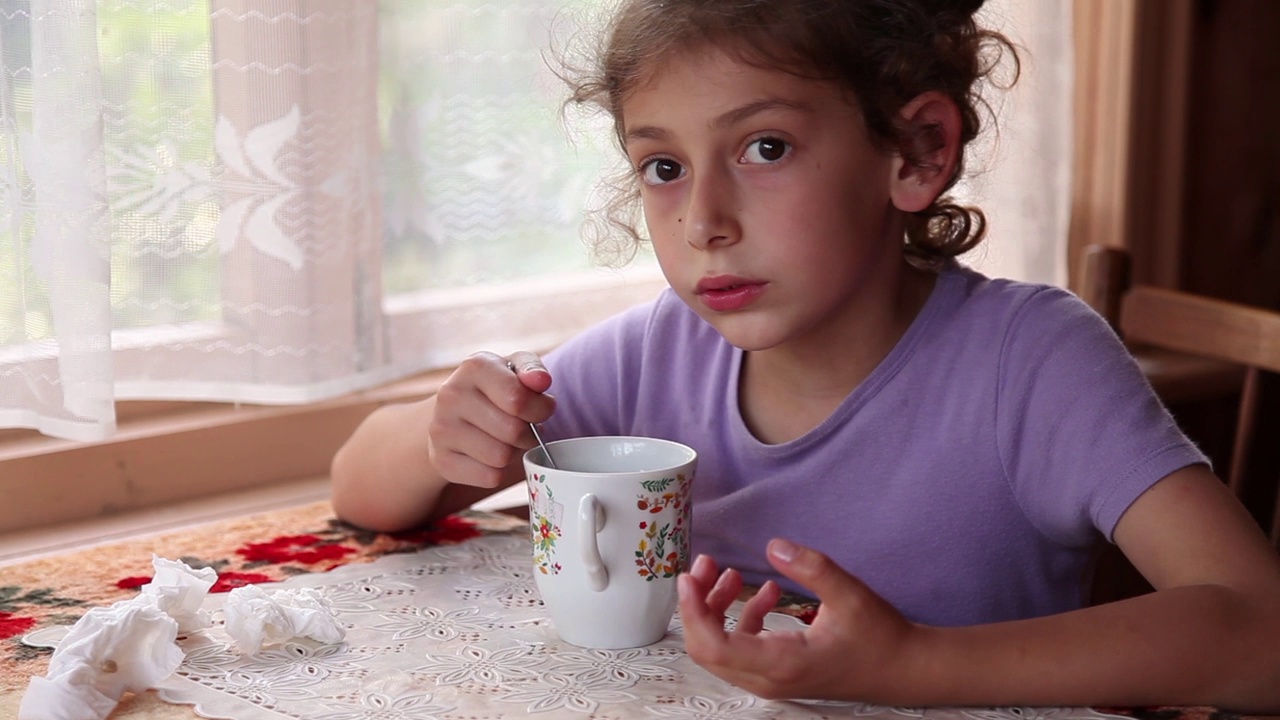 小女孩坐在靠窗的桌子旁，用茶匙喝着热茶视频下载