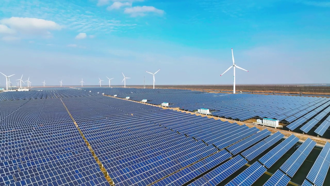 江苏省盐城市地处沿海平原，拥有大面积的太阳能光伏电站。一座高大的风力涡轮机矗立在远处。中国江苏省。视频下载