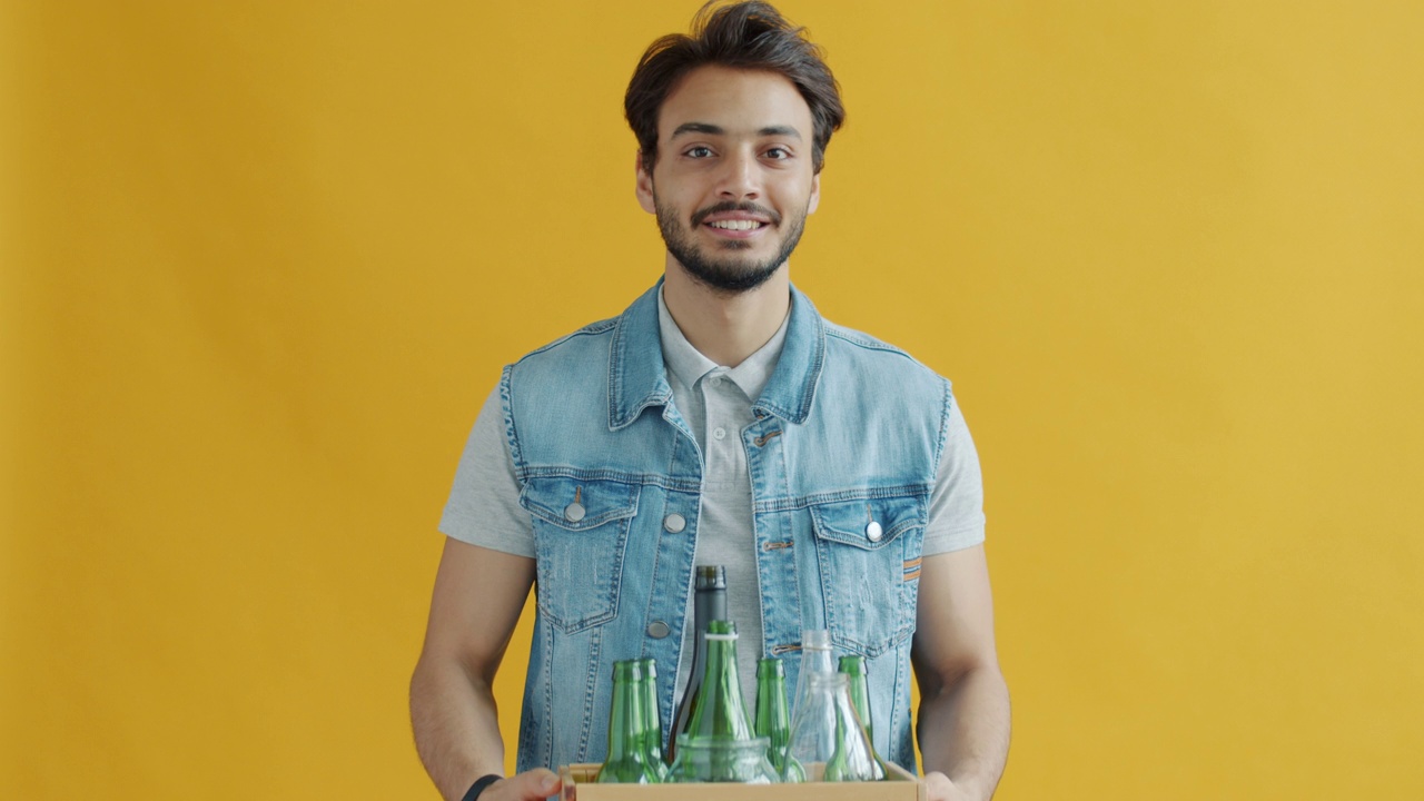 一名中东男子手持装有回收标志的玻璃瓶盒子的慢镜头肖像视频下载