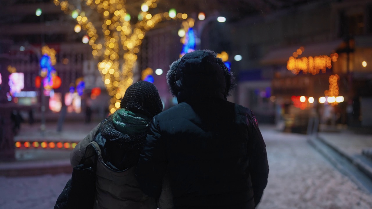 年轻的夫妇走在城市，而在下雪的冬天的晚上视频素材
