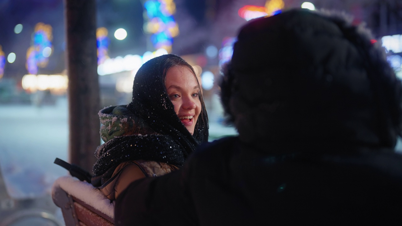 年轻的情侣约会和坐在长椅上聊天，而在城市的雪晚上视频素材