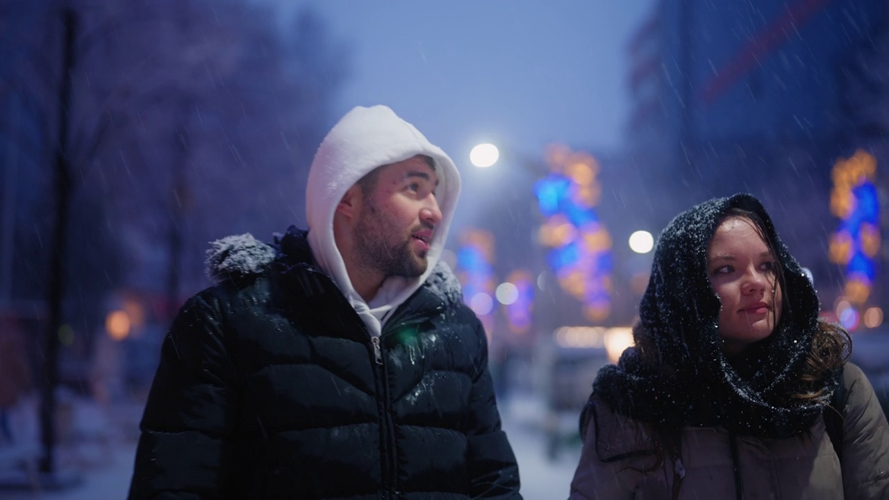 年轻的夫妇走在城市，而在下雪的冬天的晚上视频下载
