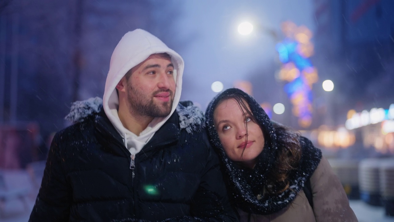 年轻的夫妇走在城市，而在下雪的冬天的晚上视频素材