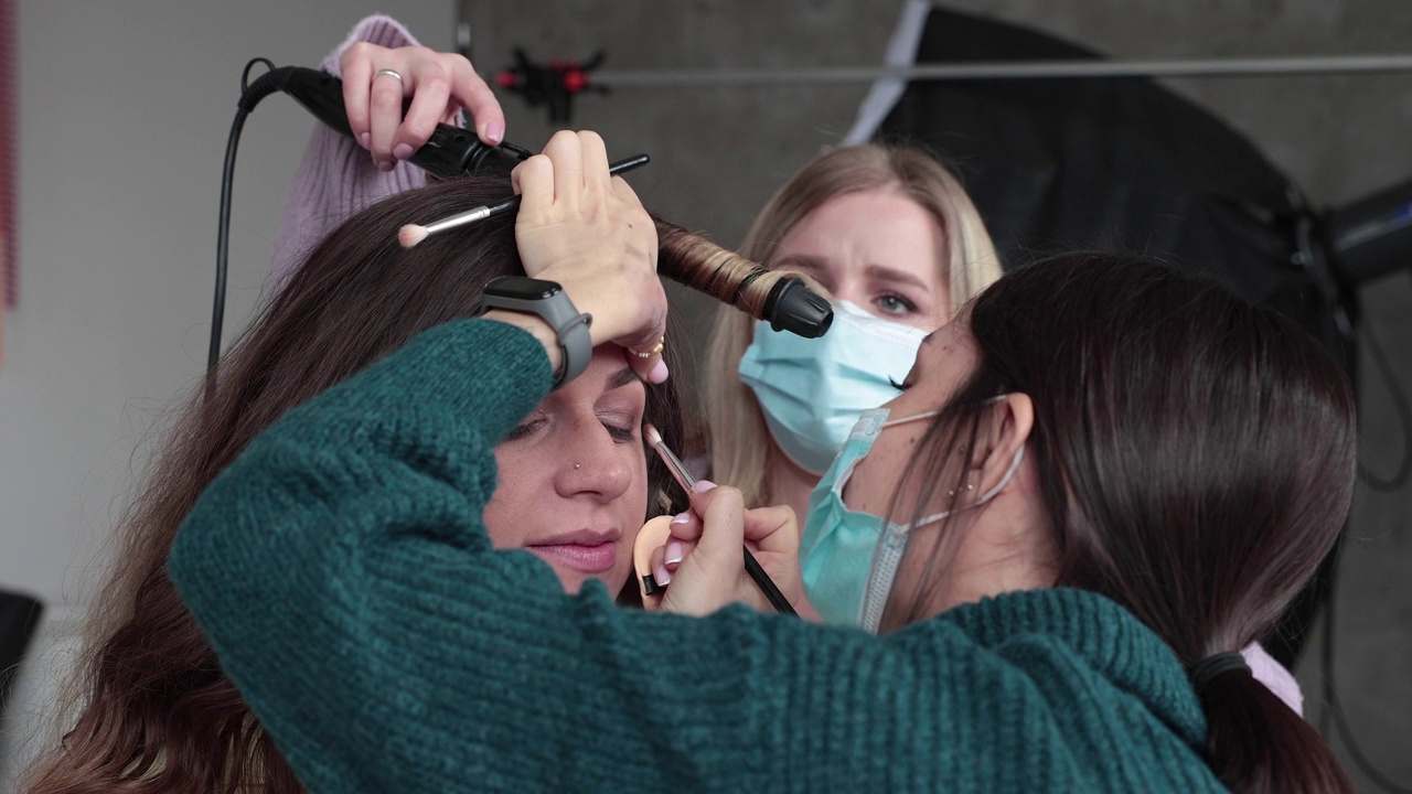 化妆师和发型师在工作室拍摄前与时装模特一起工作。视频下载