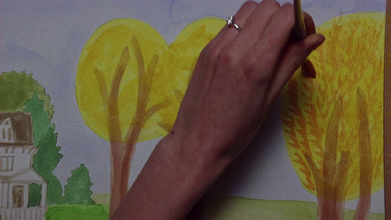 女人与钻石戒指在她的手与水彩画，添加简单的橙色叶子圆黄色的树的近角度。油漆包括房子，更多的树。视频下载