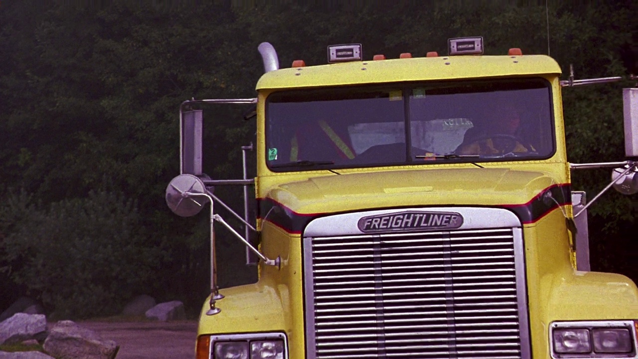 一辆大的黄色拖车拖着或拉着一辆绿色和白色的rv，旁边写着橙色的文字。树林或森林作为背景。树。Rv被泥浆覆盖。视频下载