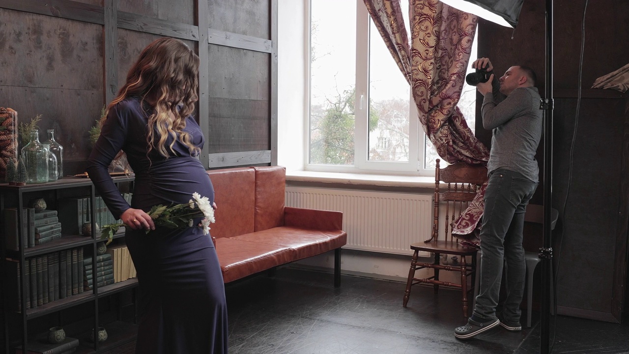 专业摄影师在摄影棚为怀孕的模特拍照。视频下载