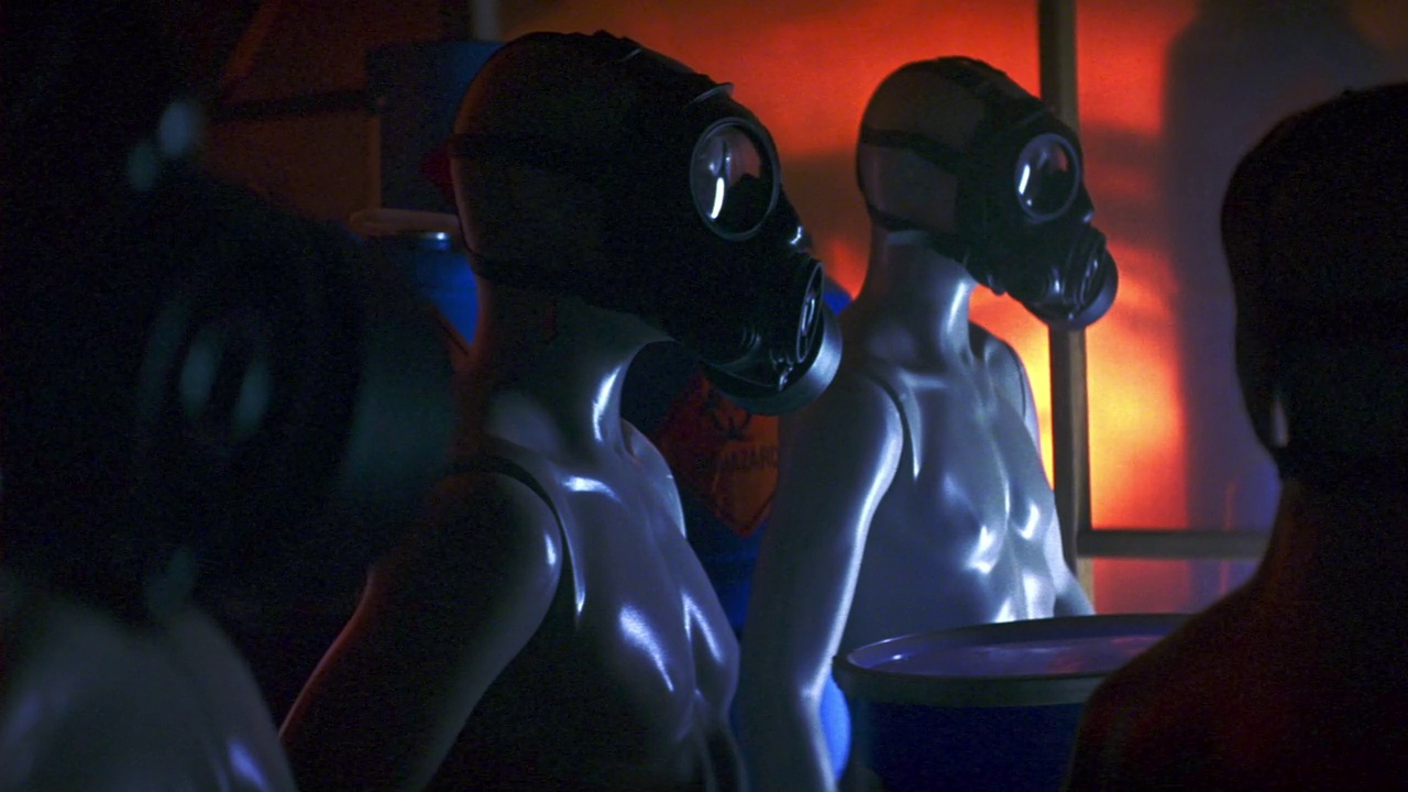 中角建立几个人体模型与防毒面具覆盖他们的脸，站在毒气室或储藏室。看到模糊的窗口背景与橙色色调的光。视频下载