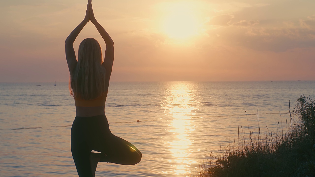 在夏日的夕阳下，以大海为背景，女人们正在做瑜伽。热身，健康生活，放松和户外运动。健康，真实，平衡和冷静的感觉。视频购买