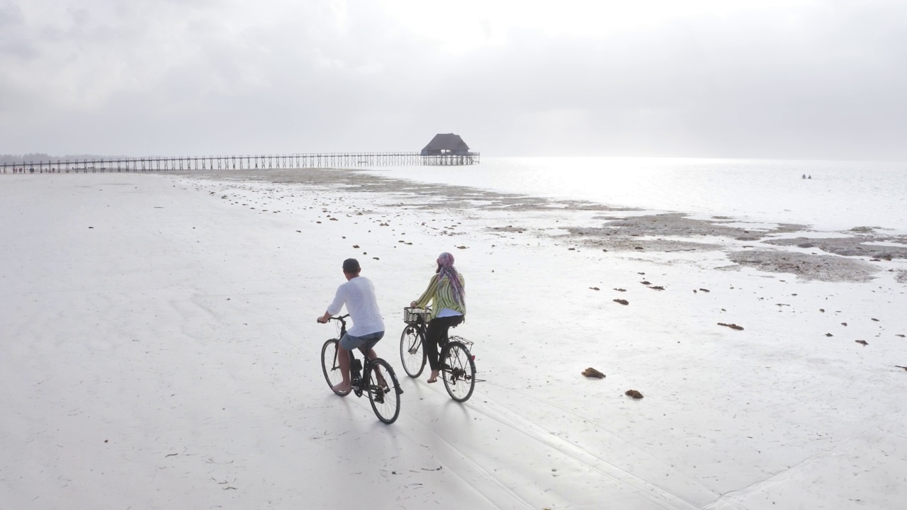 4K无人机拍摄到一对夫妇在桑给巴尔岛废弃的海滩上骑自行车。国外旅游及旅游概念。视频素材