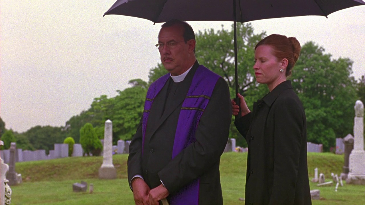 牧师或牧师站在黑色雨伞下的角度，由妇女撑着。雨天,葬礼。公墓,墓地。哀悼者在仪式结束后鱼贯而入。视频下载