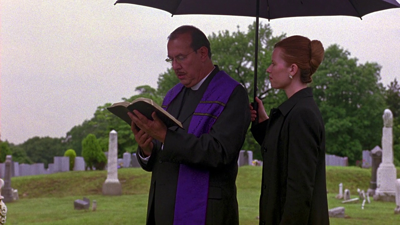 牧师或牧师站在黑色雨伞下的角度，由妇女撑着。雨天,葬礼。公墓,墓地。牧师朗读圣经。视频下载