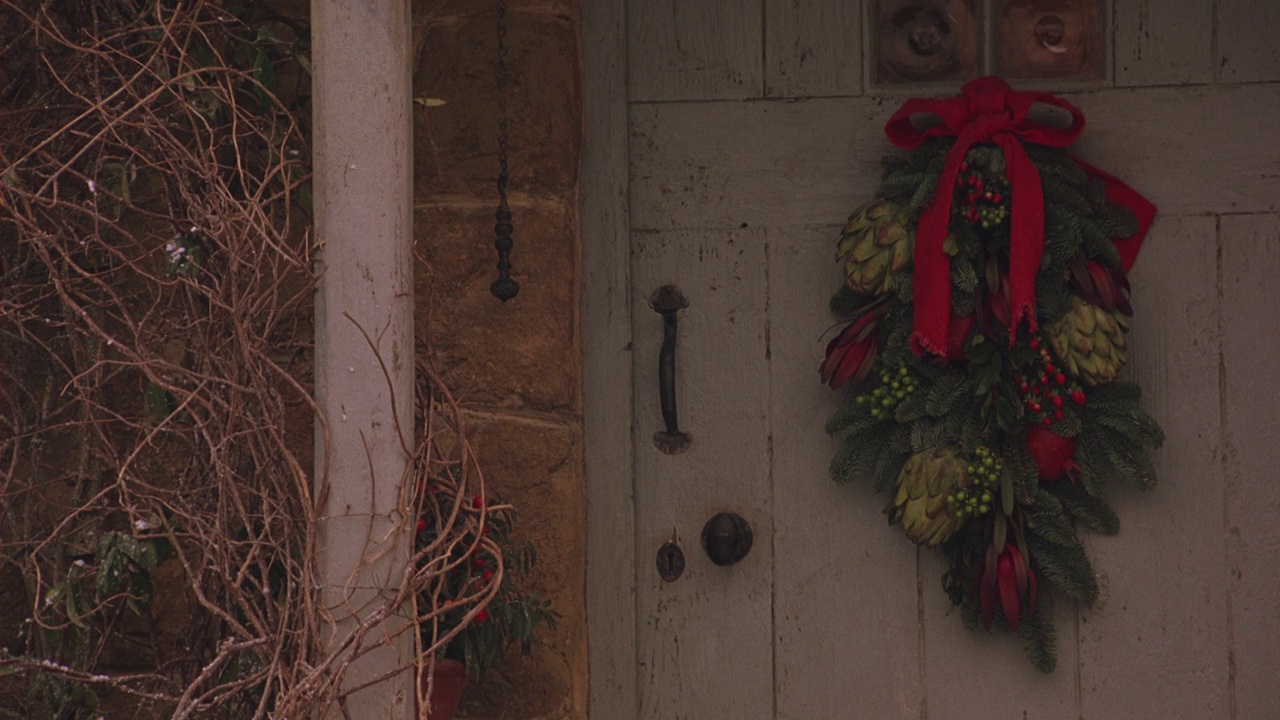 中角的前门到砖房，家，或农舍。光秃秃的常春藤挂在门左边的柱子上。蓝色的门上挂着圣诞节或节日的花环。门上的黑色钢把手。小木屋。视频下载