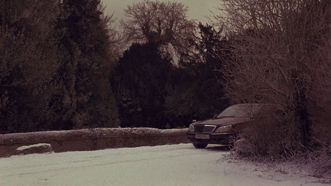 广角的雪覆盖的道路在农村。树木、低矮的岩壁、十字形墓碑的墓地。黑色奔驰车到达。视频下载