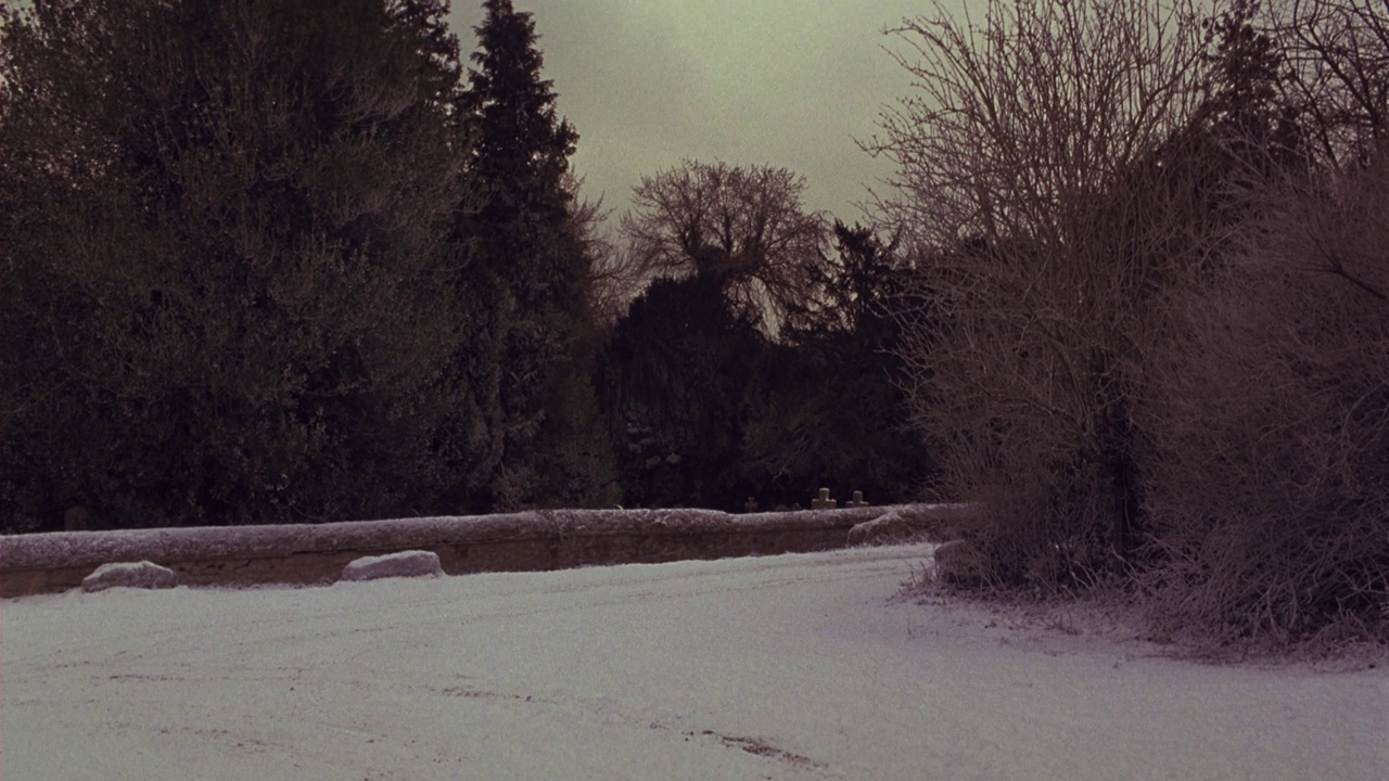 广角的雪覆盖的道路在农村。树木、低矮的岩壁、十字形墓碑的墓地。看到一辆黑色奔驰车离开。视频下载