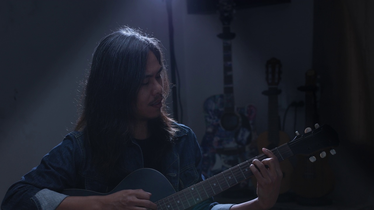一位亚洲音乐家一边弹着原声吉他，一边唱歌视频下载