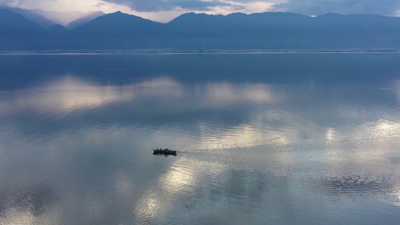 当人们在蓝色的湖面上划着小木船时，云朵和山峦倒映在水中视频素材