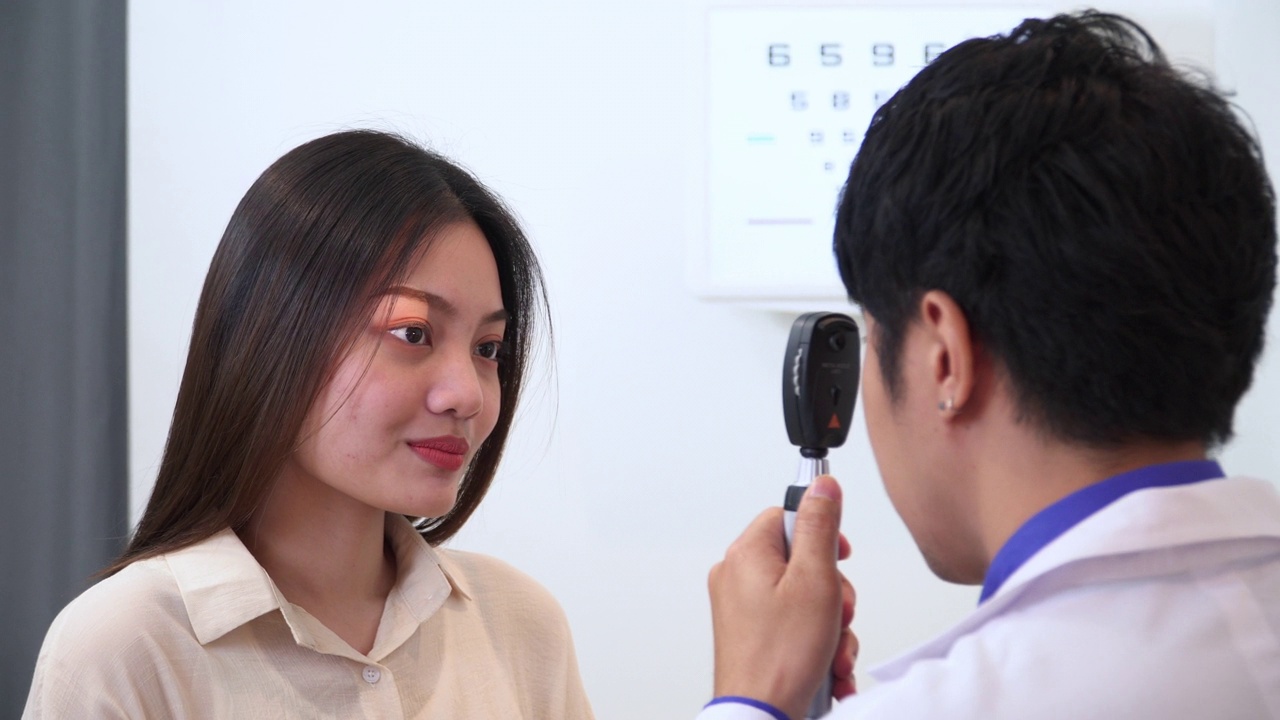 验光师使用视网膜镜和主观折射测试亚洲年轻女性的视力，准备配眼镜，表达积极的情绪，微笑以获得更好的视力视频下载