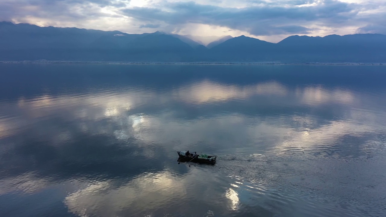 当人们在蓝色的湖面上划着小木船时，云朵和山峦倒映在水中视频素材