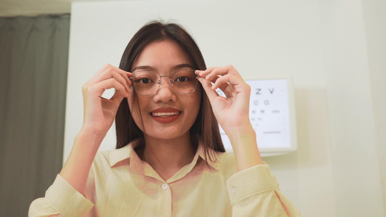肖像:亚洲年轻女性在诊所试用新的光学眼镜，通过新的眼镜更好的视力，看着相机作为镜子视频下载