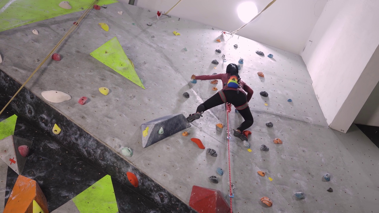 女性穆斯林攀岩者攀岩墙与安全安全带室内健身房视频下载