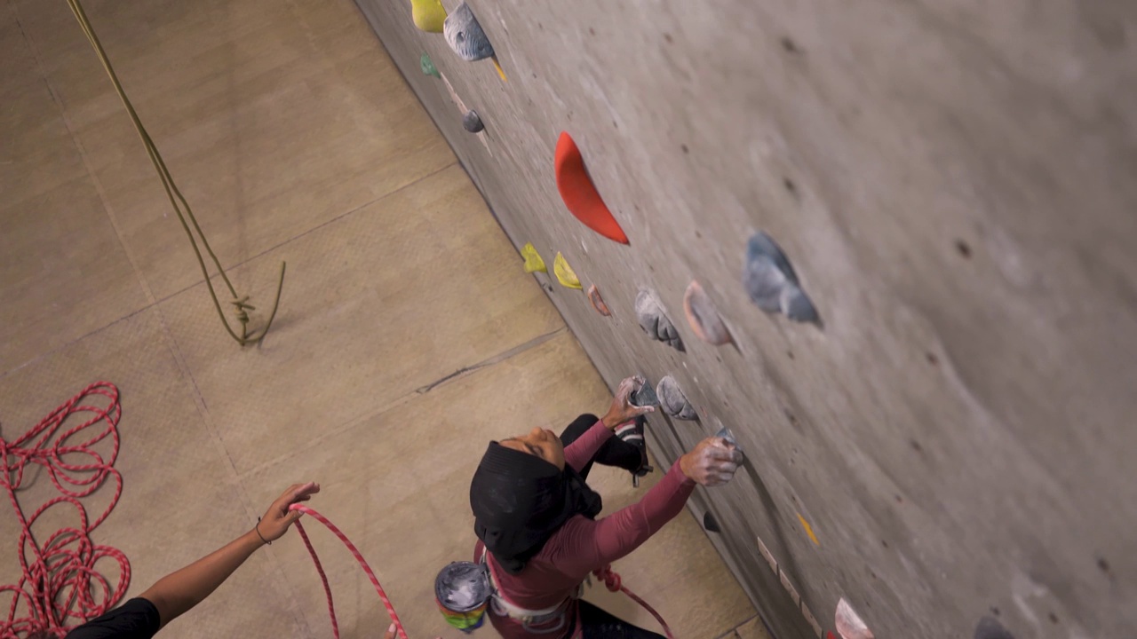 女性穆斯林攀岩者攀岩墙与安全安全带室内健身房视频下载