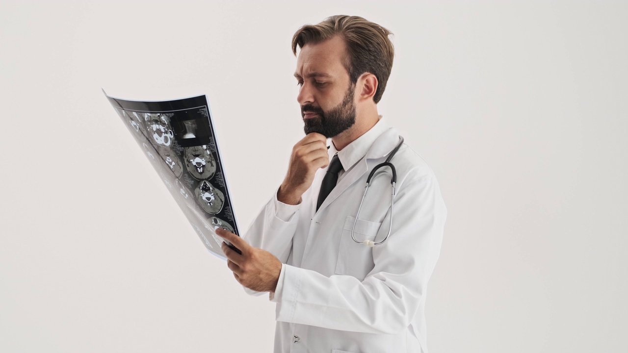 严肃的男医生拿着听诊器，一边认真地看着x光片，一边思考和摸着自己的胡子视频下载