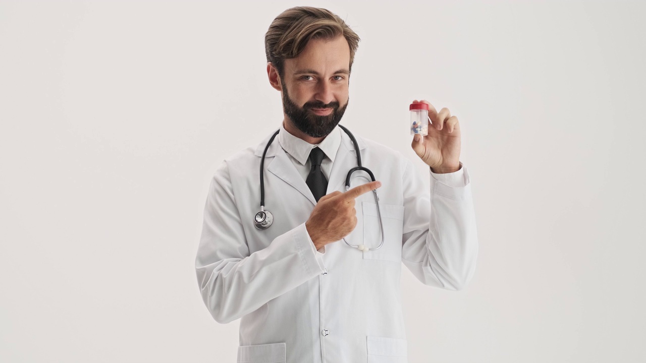帅哥医生拿着听诊器微笑着用手指指着瓶子里的药丸视频下载