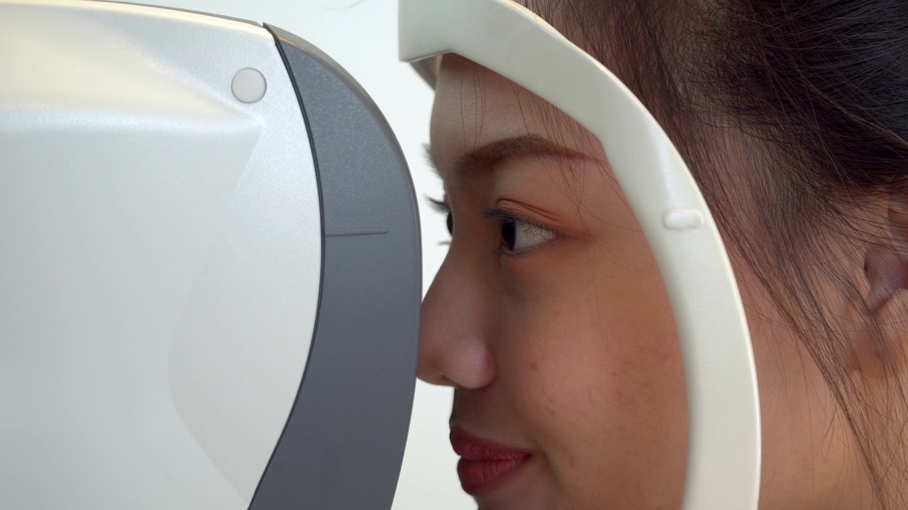 特写:亚洲年轻女子在眼科医生的办公室用专业设备检查她的视力视频下载