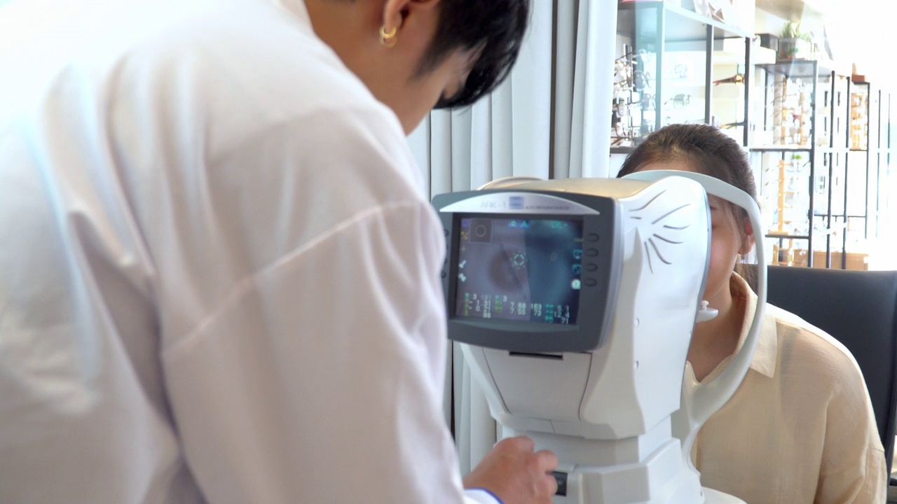 亚洲年轻女子在眼科医生的办公室被专业设备检查她的视力，由电脑监控，准备制作光学眼镜，看后肩视频下载