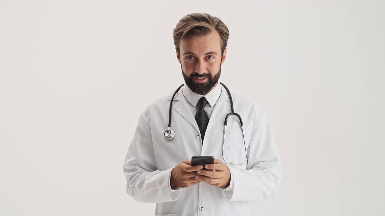 英俊的男医生带着听诊器用智能手机微笑着视频素材