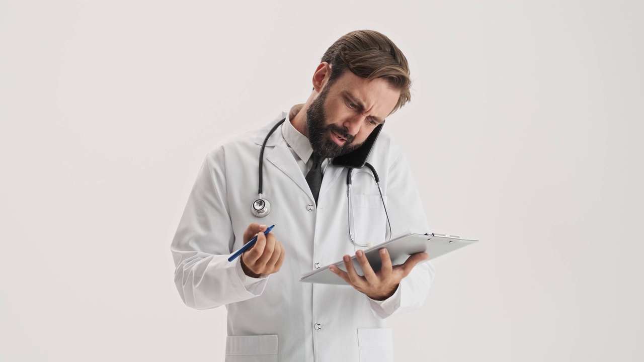 不高兴的男子医生与听诊器工作的病史和通话的智能手机视频下载