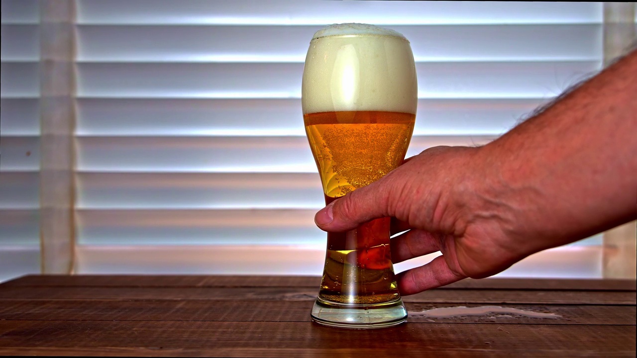 男子的手正从潮湿的木桌上的玻璃杯里拿着啤酒视频下载