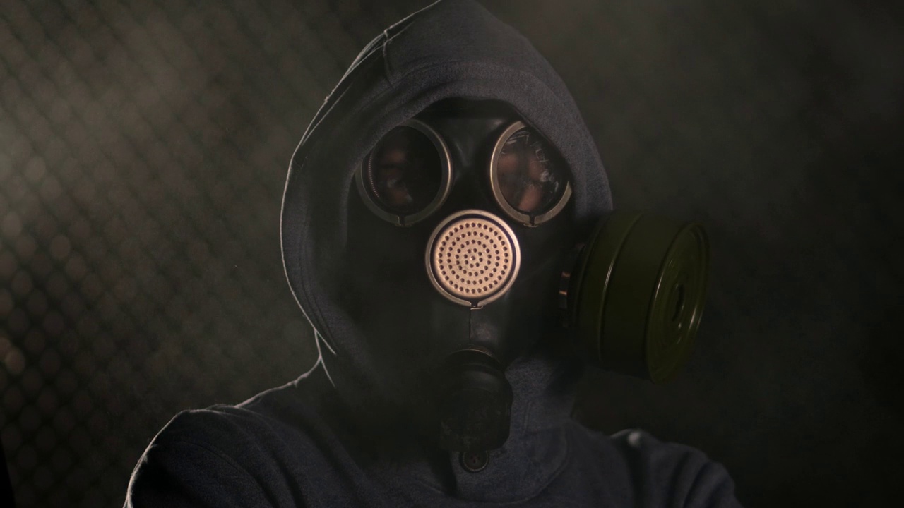 黑暗中一个戴着防毒面具和兜帽的男人的肖像。烟雾正在他周围扩散视频下载