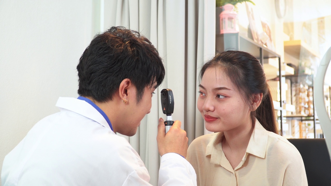 验光师调整视网膜镜和主观折射的距离，测试亚洲年轻女性的视力，准备配眼镜，表达积极的情绪，微笑以获得更好的视力视频下载