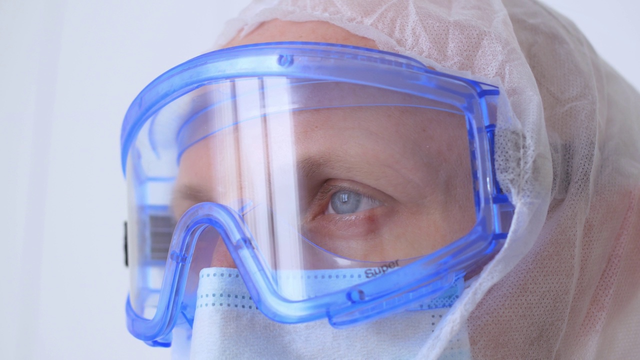 一个戴着防护面罩和眼镜，穿着无菌服的医生疲惫的眼睛的特写。一名卫生工作者在有冠状病毒患者的地区辛苦工作了一天。病人的治疗视频素材