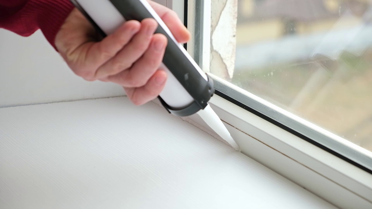 一名男子应用密封胶接缝之间的窗口和窗台从一个管硅酮密封胶与枪嵌缝。视频素材