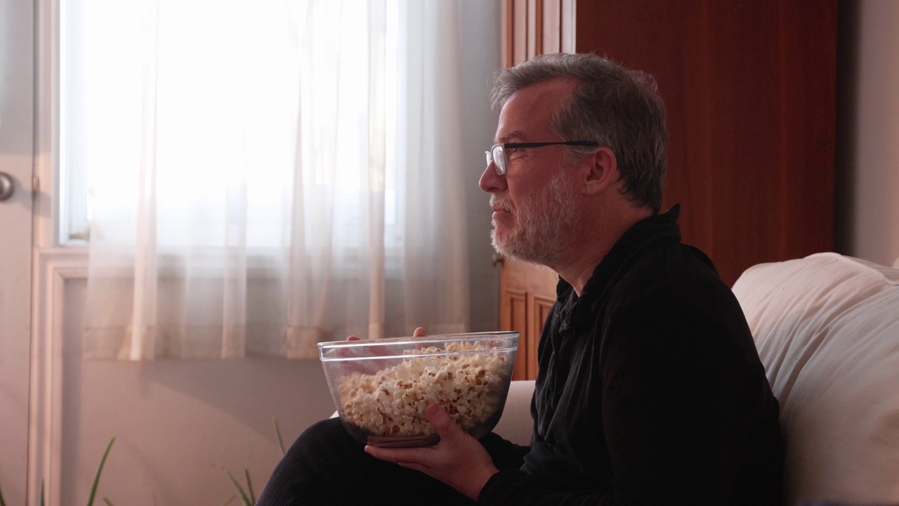 一个成熟的男人拿着爆米花坐着，用语音激活启动电视节目视频下载
