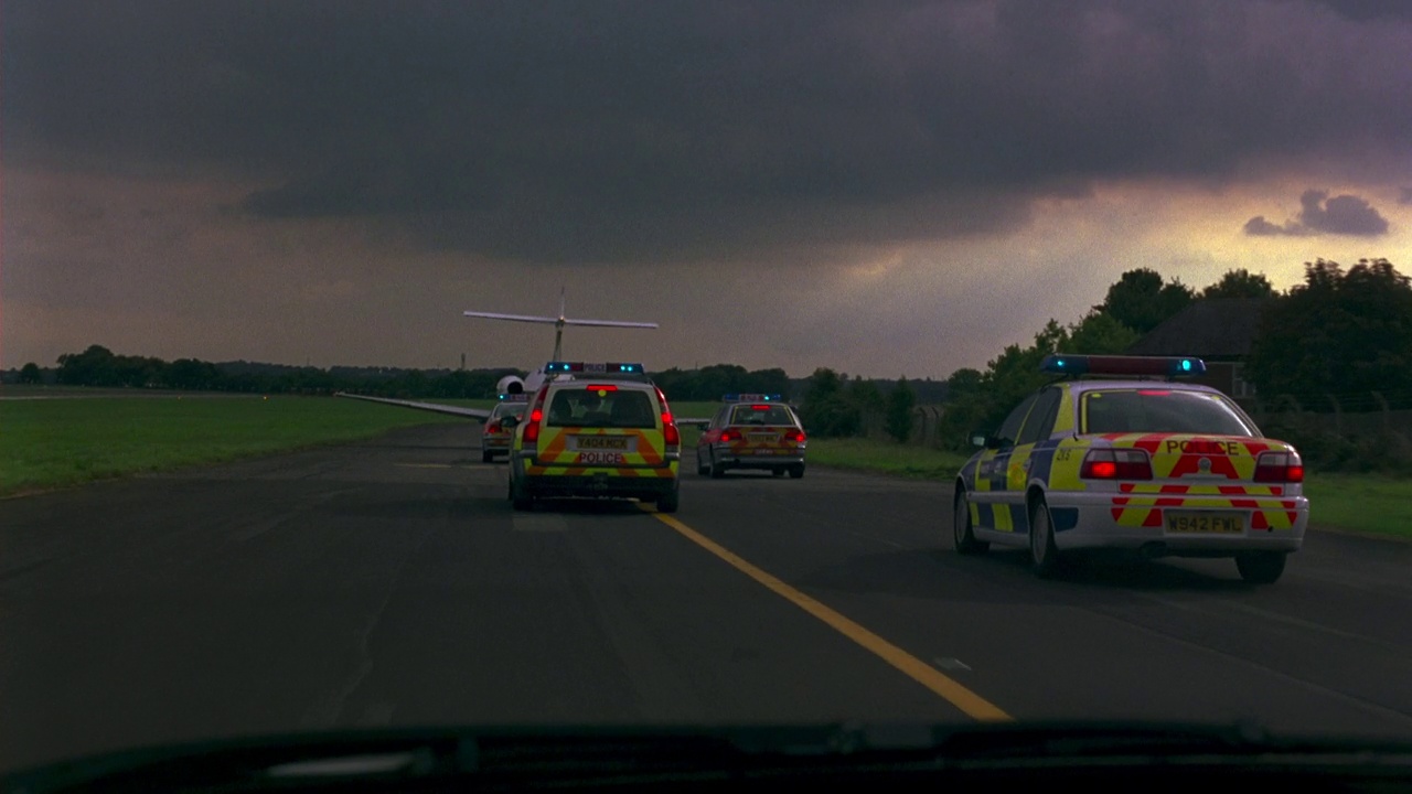 广角驾驶镜头直直地在警车驶进机场跑道前。几辆英国交通警车驶过一个小机场，经过“紧急服务集合点”的标志上了停机坪。闪着灯的警车视频下载