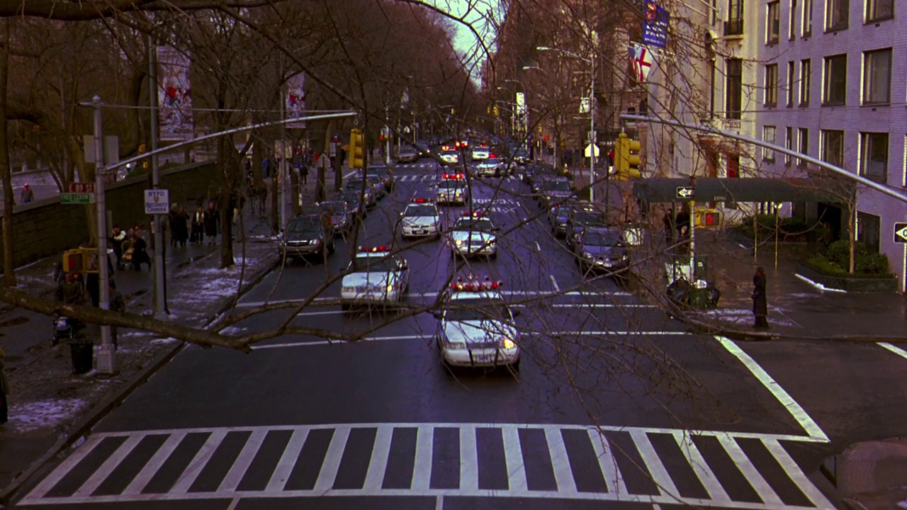 纽约市街道上汽车行驶的广角镜头。行人走在积雪覆盖的人行道上。人行道。当警车闪烁着警灯、警笛、警笛在街道上高速行驶时，镜头从高角度向下平移。警车停在a街视频素材