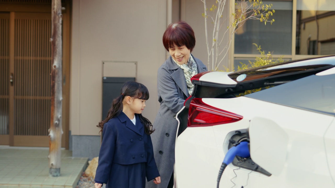 MS-一个年轻的女孩正在帮助她的祖母从他们的电动汽车上卸下购物的东西视频下载